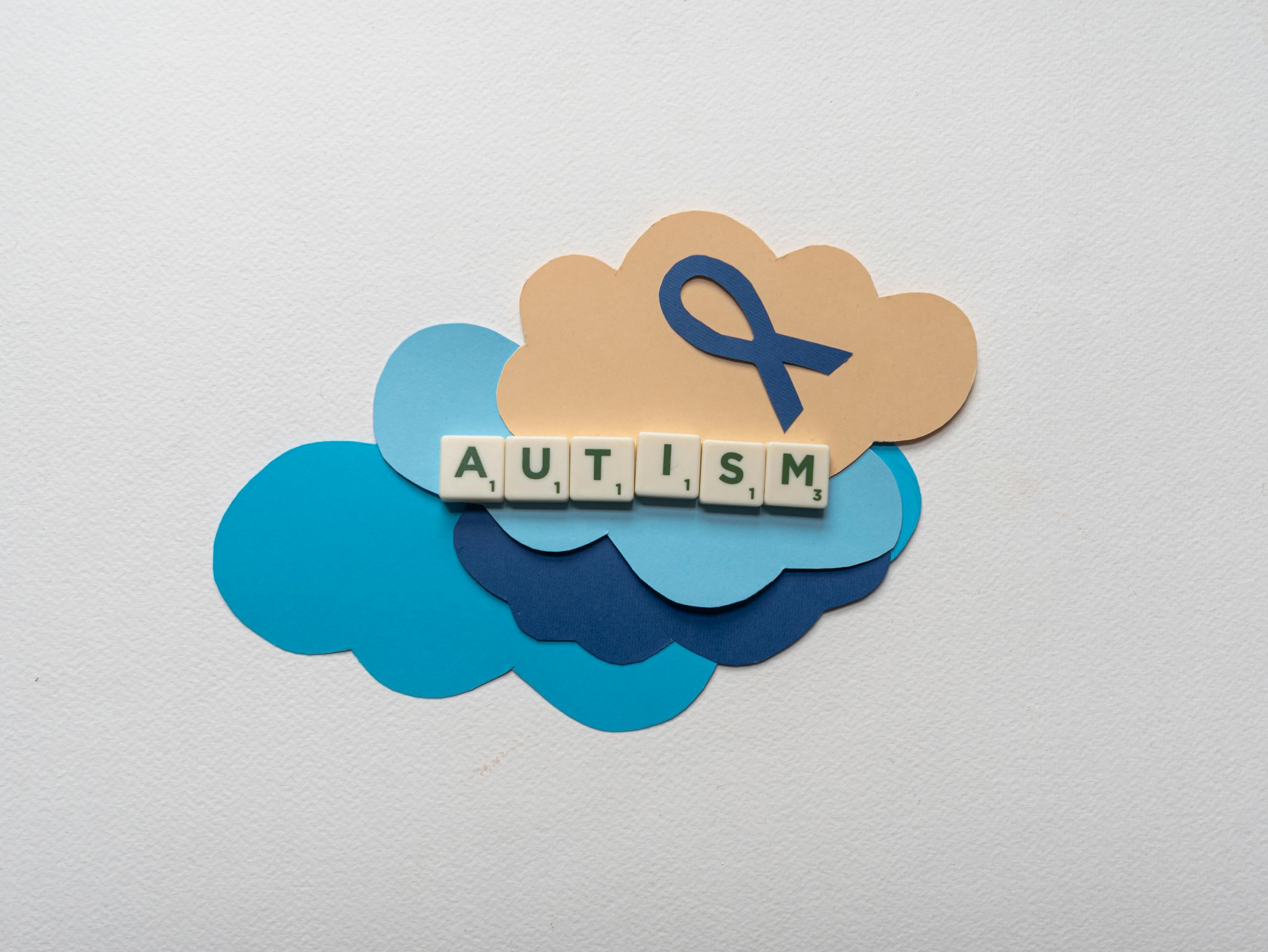 Creative representation of autism awareness using scrabble tiles on colorful clouds and ribbon.