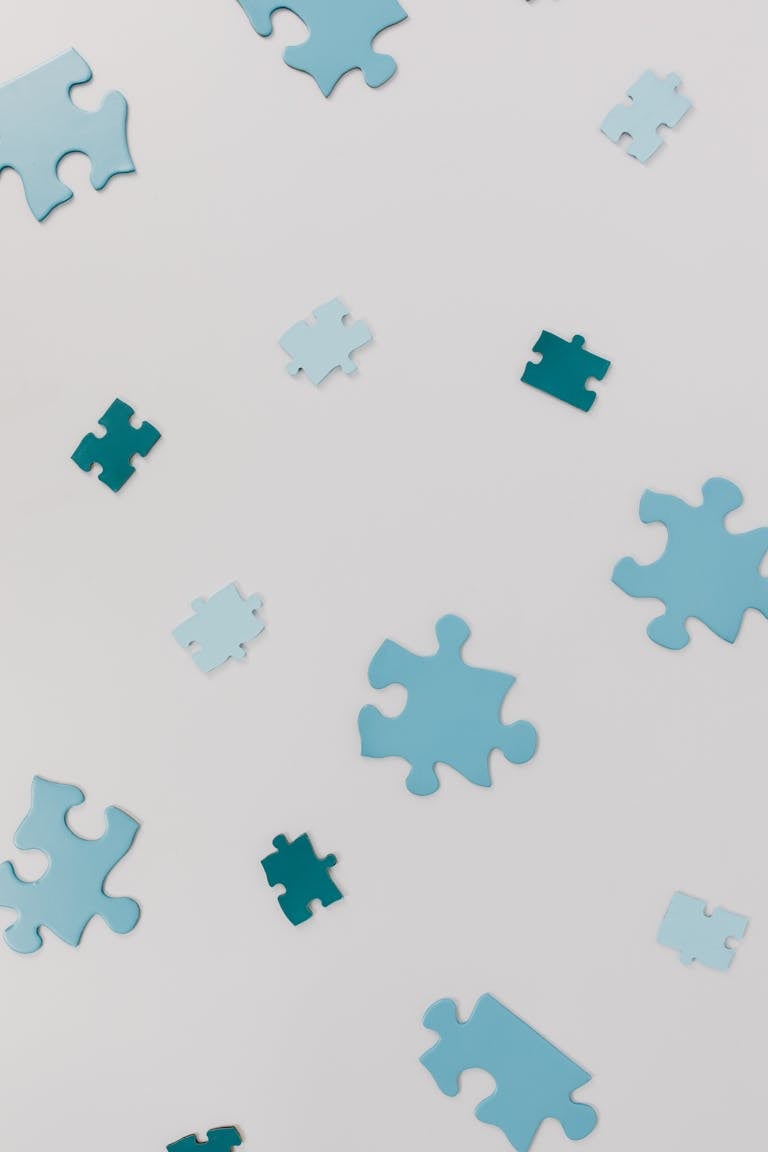 Close-up of varied blue puzzle pieces scattered randomly on a white surface.