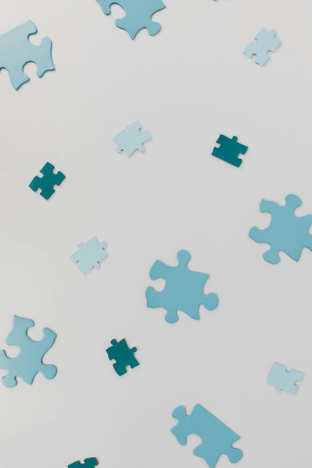 Close-up of varied blue puzzle pieces scattered randomly on a white surface.