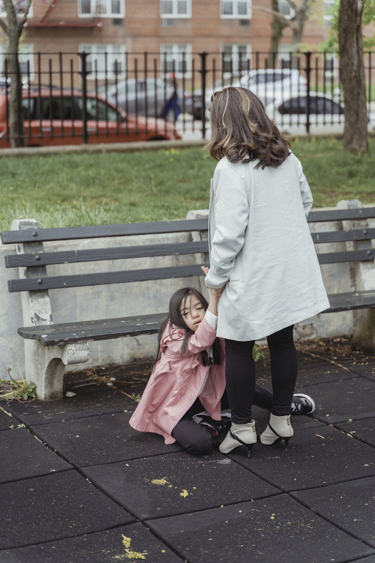 A mother assists her child having a tantrum on a park bench outdoors.