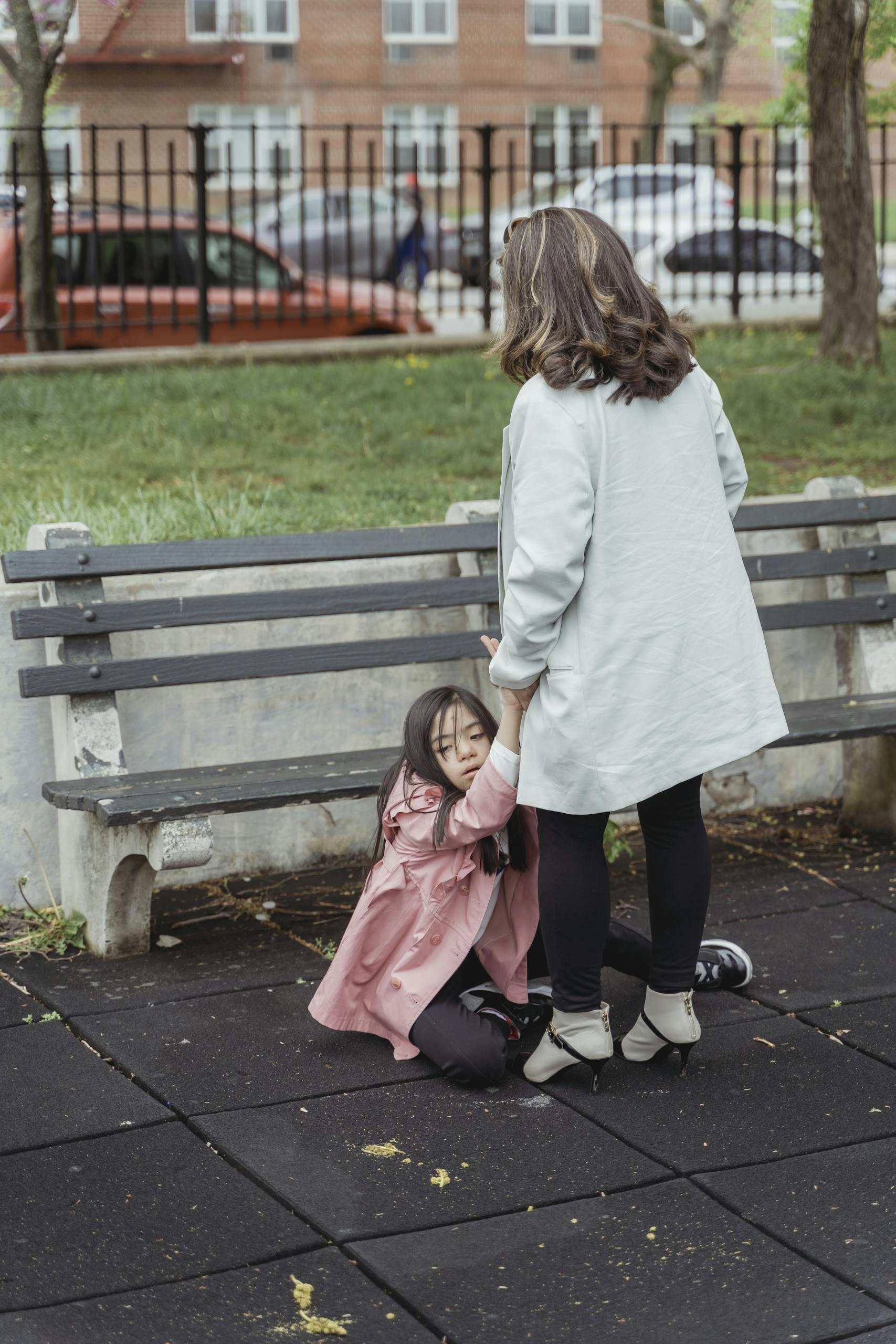 A mother assists her child having a tantrum on a park bench outdoors.