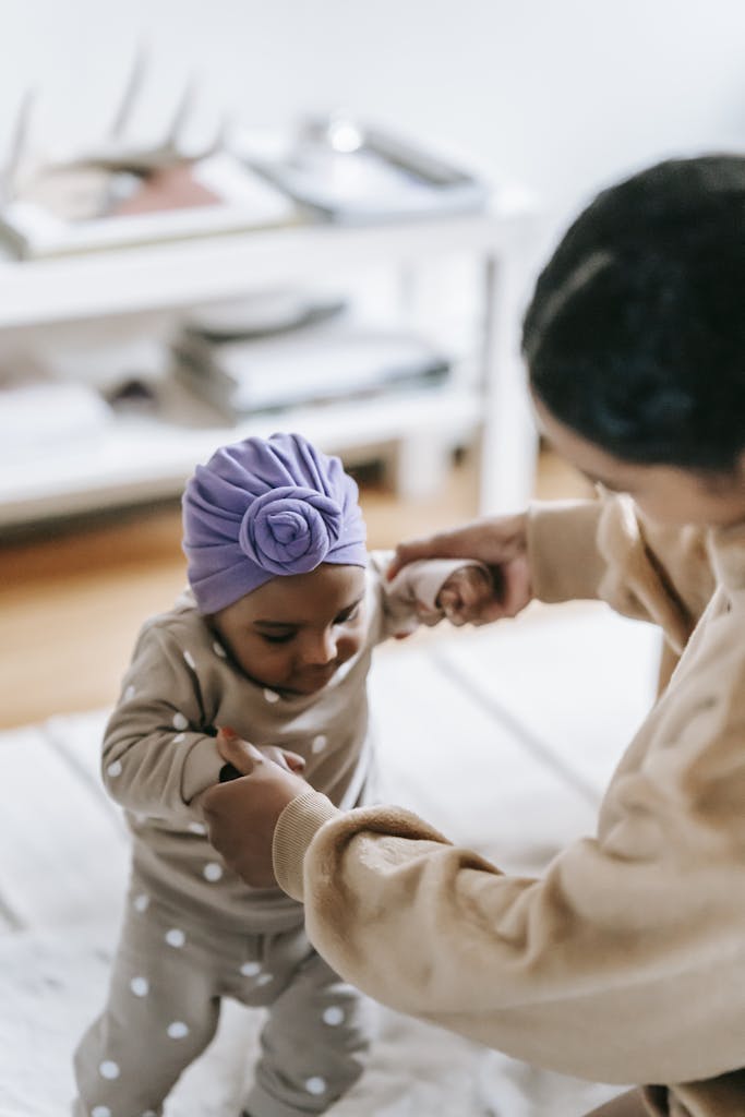 A mother supports her baby as they take their first steps at home, showcasing family bonding.