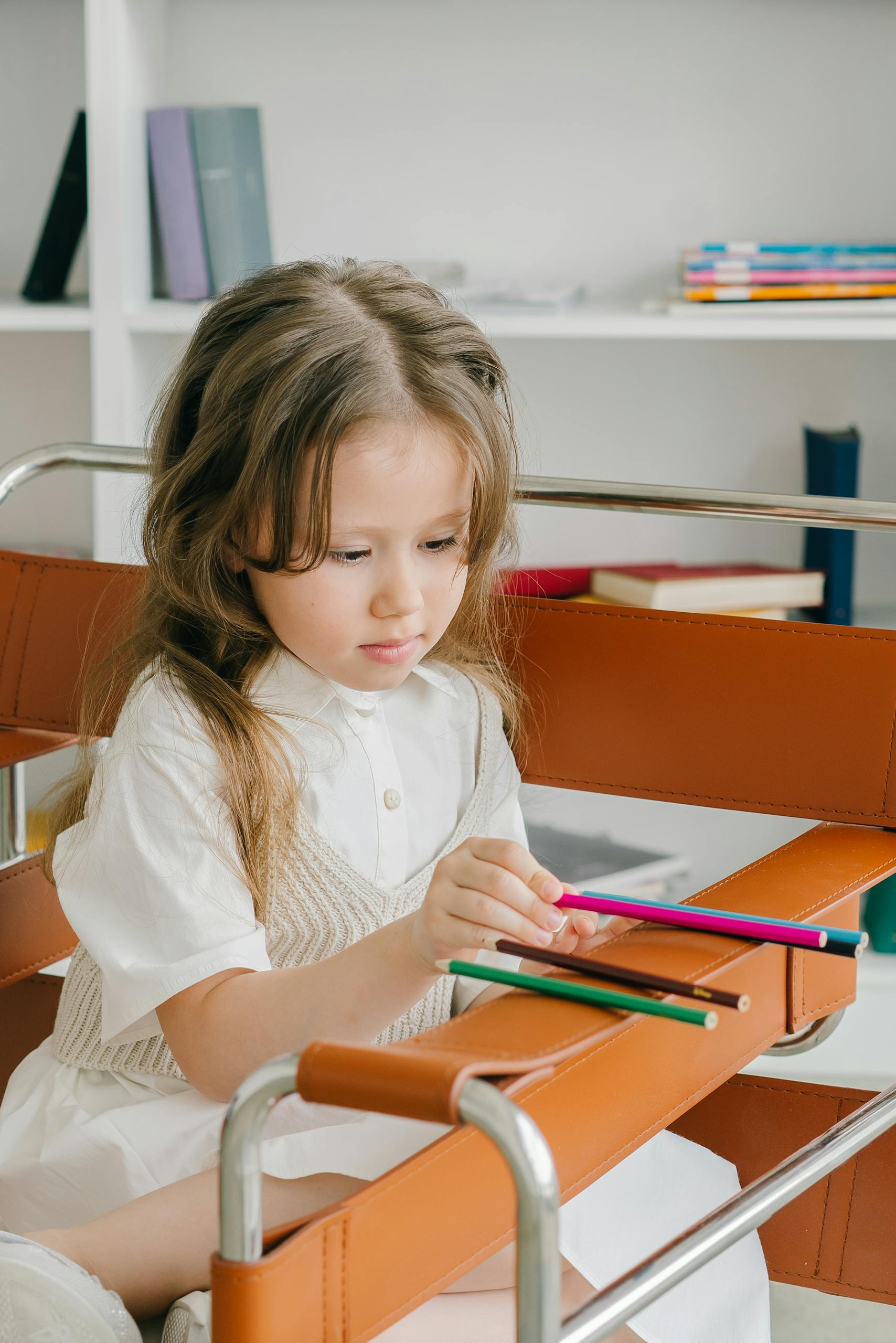 A young girl sits on a chair drawing with colored pencils, focused and serene.