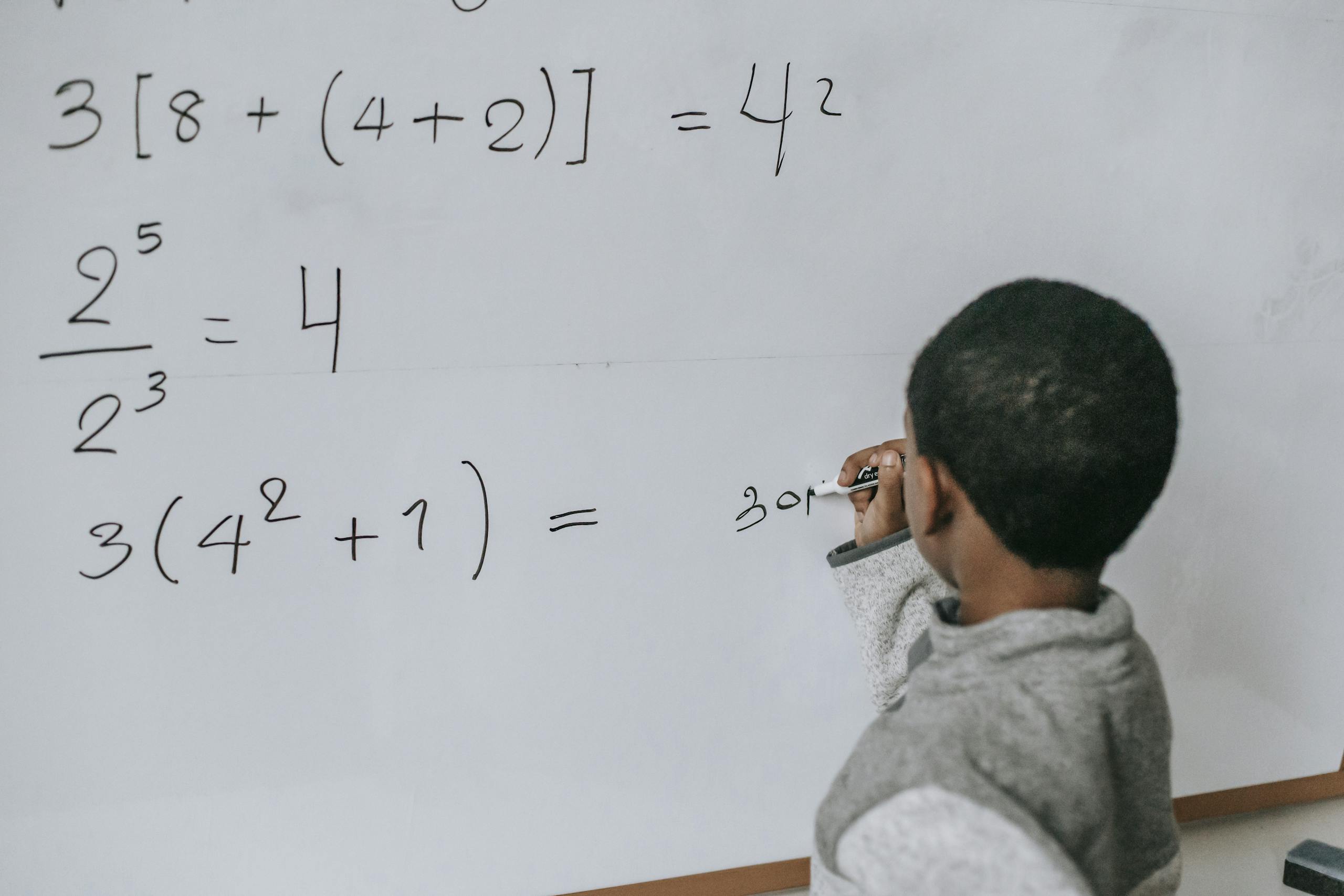 Focused child solving equations on a whiteboard, showcasing education and problem-solving skills.