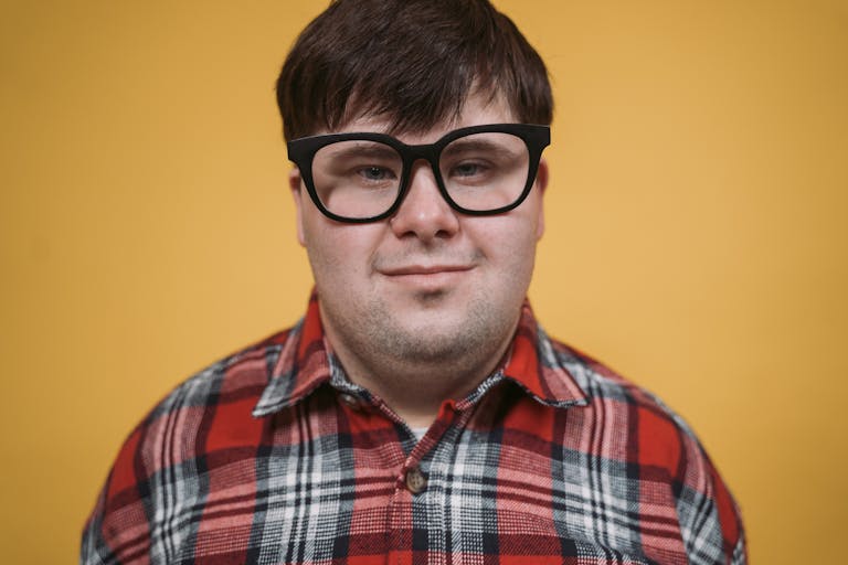 Portrait of a man with glasses wearing a red plaid shirt, set against a yellow backdrop.