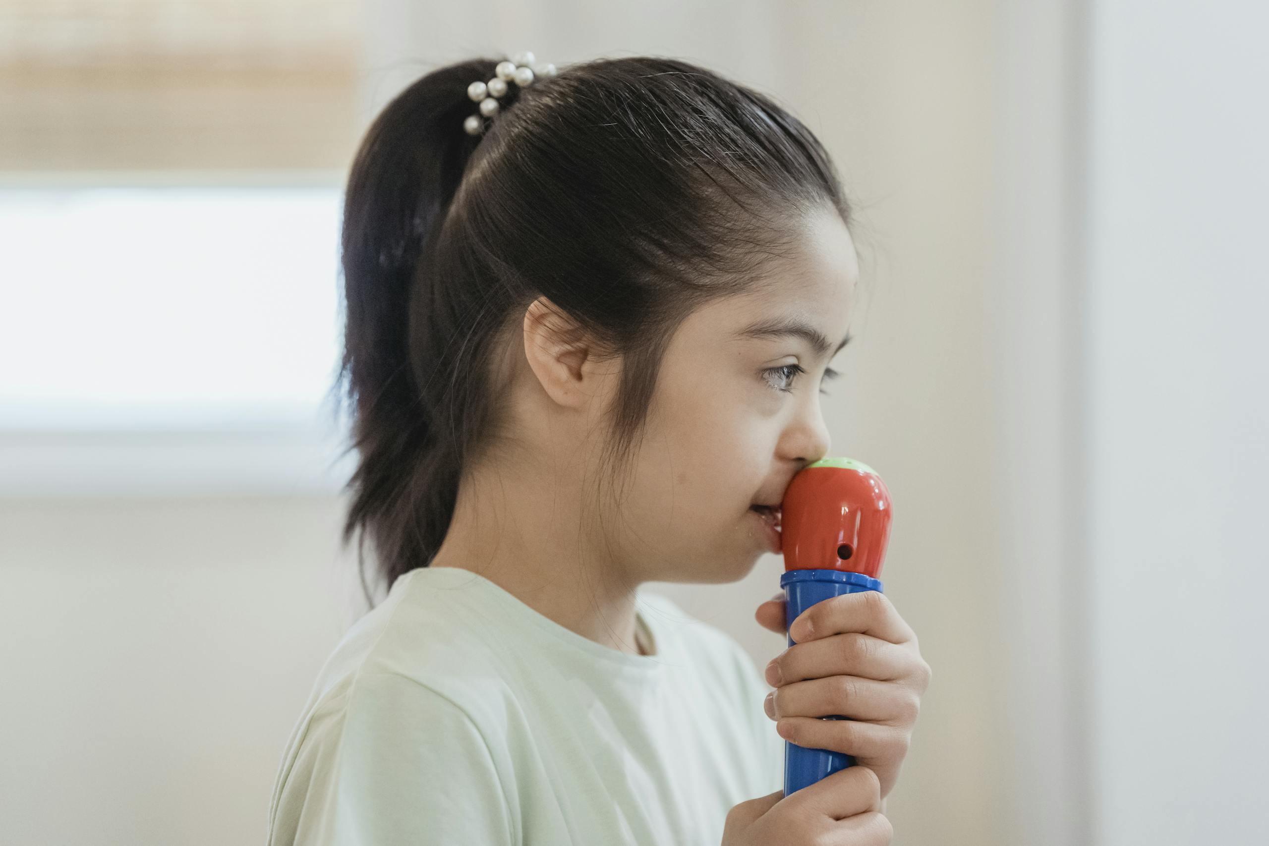 Side view of a young girl with Down syndrome engaging with a toy microphone.