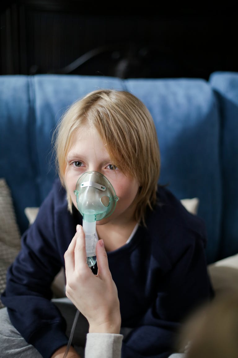 Young child sitting on a sofa while receiving inhalation therapy indoors.