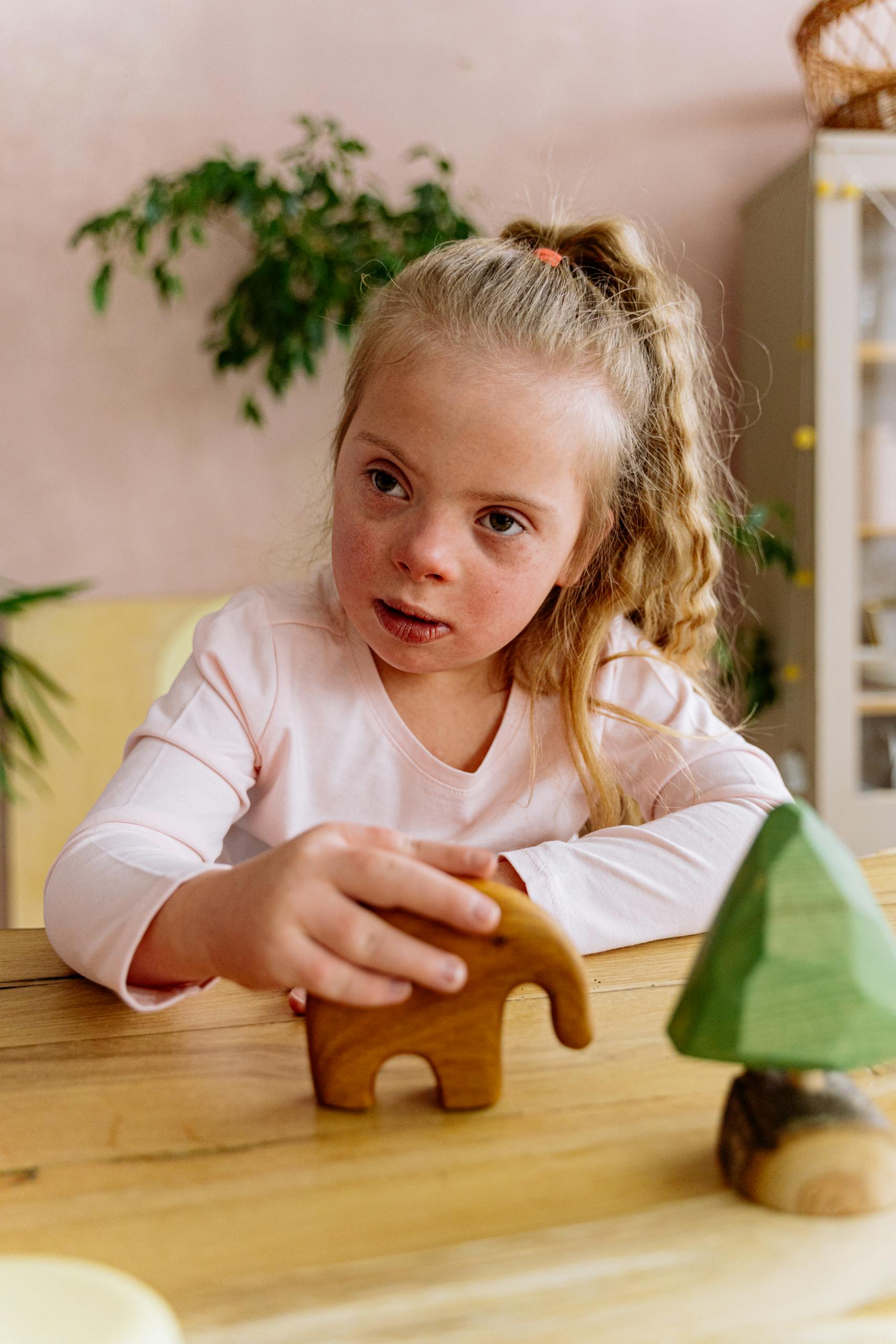 Young girl with Down Syndrome happily plays with wooden toys at a table indoors.