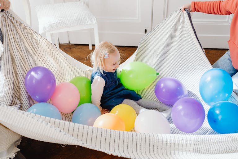 A cheerful young girl laughing while surrounded by vibrant balloons indoors.