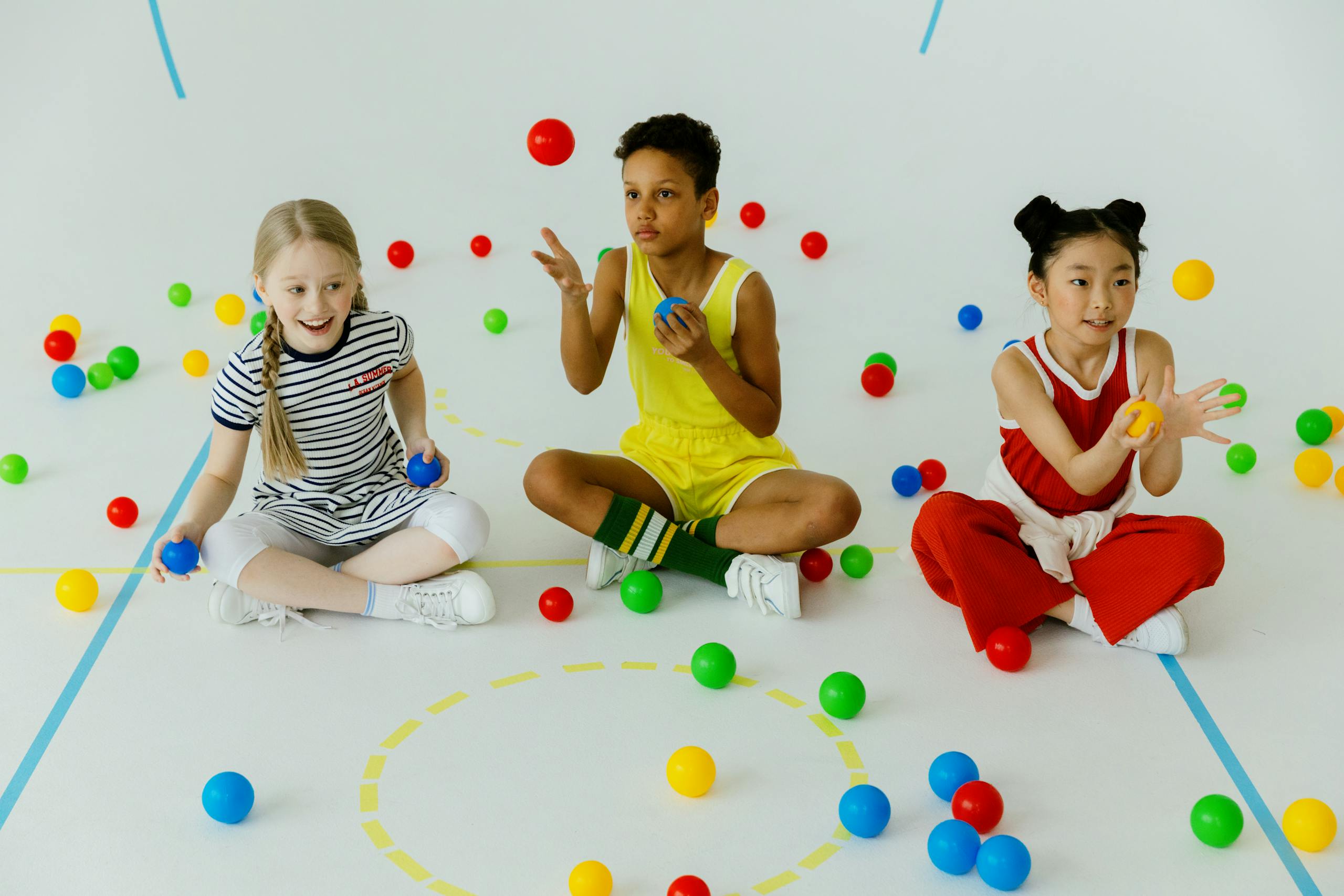 Three children of diverse backgrounds play with colorful balls indoors, showcasing fun and creativity.